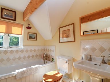 A bathroom with a bathtub a toilet and a sink under a slanted ceiling at Highgrove Barn in Painswick