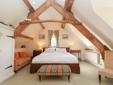 A bedroom with a bed sofa ottoman and wooden beams at Highgrove Barn in Painswick