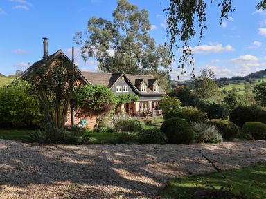 A countryside house with a garden and outdoor seating surrounded by trees and hills at Highgrove Barn in Painswick