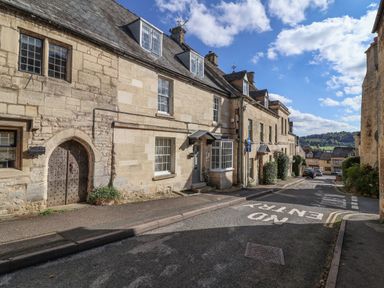 A street with stone buildings and parked cars under a blue sky at Highgrove Barn in Painswick