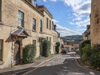 A narrow street with stone buildings and cars parked on the side at Highgrove Barn in Painswick