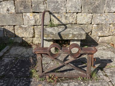 A rusted metal tool with two circular openings on a stone pavement against a stone wall at Highgrove Barn in Painswick