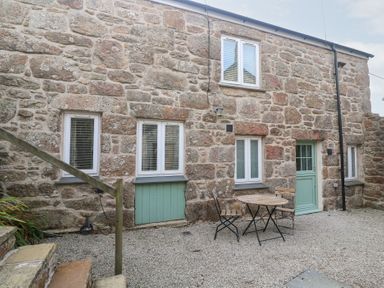 An outdoor area with a stone wall and a table with chairs at Mys Hedra Farm St Buryan