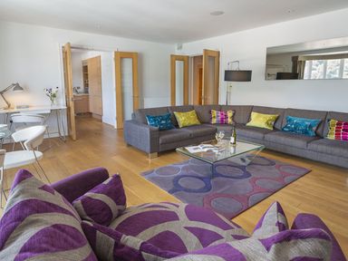 A living room with a gray sectional sofa with colorful pillows a purple patterned armchair and a glass coffee table at 21 Dart Marina in Dartmouth