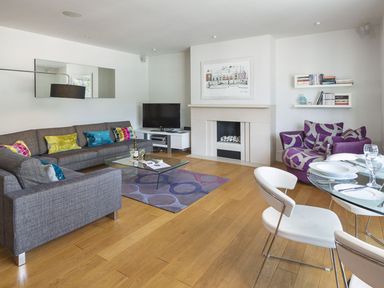 A living room with two gray sofas colorful pillows a glass coffee table a purple armchair a glass dining table with white chairs and a fireplace at 21 Dart Marina Dartmouth