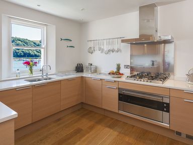 A kitchen with wooden cabinets a gas stove a window with a view of trees and water at 21 Dart Marina in Dartmouth