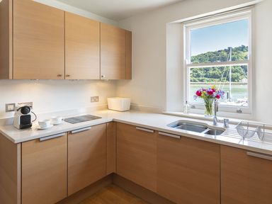 A kitchen with wooden cabinets a coffee machine a stovetop a sink and a window with flowers on the sill at 21 Dart Marina in Dartmouth