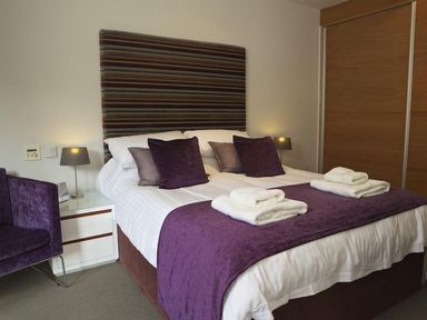 A bedroom with a double bed with white and purple bedding two bedside lamps a purple chair and wooden wardrobe at 21 Dart Marina Dartmouth