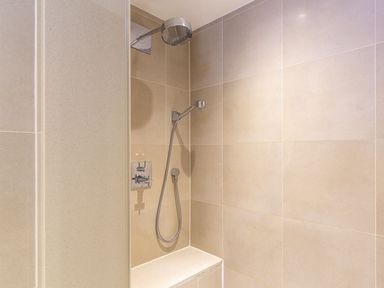 A shower area with a wall-mounted showerhead handheld shower and control knobs in a tiled bathroom at 21 Dart Marina in Dartmouth