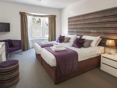 A bedroom with two beds a striped headboard purple throw blankets a chair an ottoman and a window at 21 Dart Marina in Dartmouth