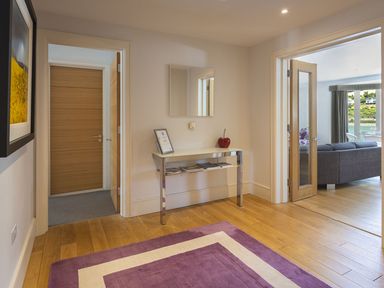 A hallway with wooden floor a purple and white rug a console table with magazines a mirror and doors leading to other rooms at 21 Dart Marina in Dartmouth