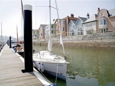 A sailboat docked alongside a wooden pier with houses in the background at 21 Dart Marina Dartmouth