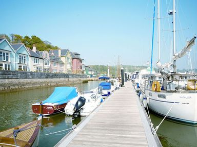 A marina with boats docked along a wooden pier and colorful houses by the water at 21 Dart Marina in Dartmouth