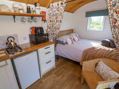 A bedroom with a bed and kitchen area at Higher Merther Farm Shepherds Hut Helston