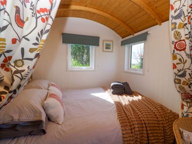 A bedroom with a bed and windows at Higher Merther Farm Shepherds Hut in Helston