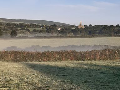A landscape with a misty field and buildings in the background at Higher Merther Farm Shepherds Hut Sithney near Helston