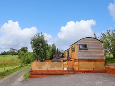 A wooden cabin with a fenced patio and outdoor seating in a rural area at The View in Bangor-On-Dee