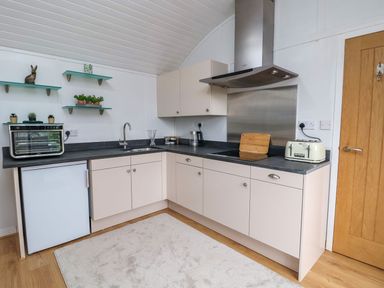 A kitchen with white cabinets black countertops a toaster cutting board a coffee maker and small plants on glass shelves at The View in Bangor-On-Dee