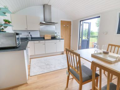 A kitchen with white cabinets wooden dining table chairs and an open door showing a garden at The View in Bangor-On-Dee
