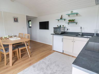 A kitchen and dining area with a wooden table and chairs a kitchenette with a sink toaster oven and shelves with plants at The View in Bangor-On-Dee