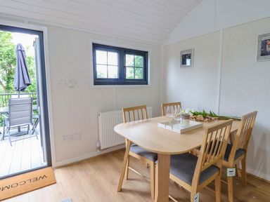 A dining room with a wooden table set with glasses flowers and a tray next to a door leading to an outdoor patio with chairs and umbrella at The View in Bangor-On-Dee