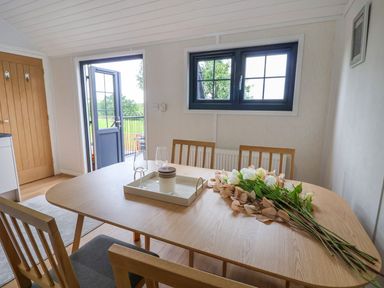 A dining room with wooden table and chairs flowers on the table and a door open to the outside at The View in Bangor-On-Dee