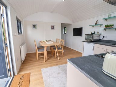 A dining area with a wooden table and chairs next to a kitchen with countertop appliances at The View in Bangor-On-Dee