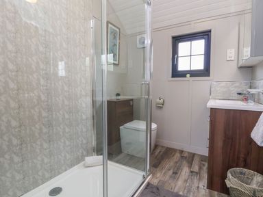 A bathroom with a shower enclosure a toilet a sink with wooden vanity a small window and wood flooring at The View in Bangor-On-Dee