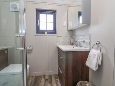 A bathroom with a wooden vanity sink a toilet a towel ring with a white towel a small window and a glass shower door at The View in Bangor-On-Dee