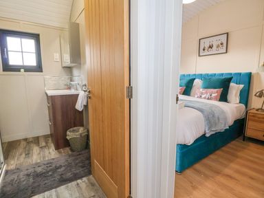 A partially open door showing a bathroom with sink and a bedroom with a bed and artwork at The View in Bangor-On-Dee