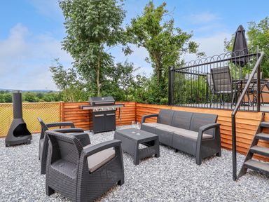 An outdoor seating area with black wicker furniture a grill and a patio with table and umbrella at The View in Bangor-On-Dee