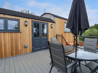 A patio area with a glass table and four chairs outside a wooden building with double doors at The View in Bangor-On-Dee