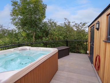 A wooden deck with a hot tub a storage box and a red hose attached to a building at The View in Bangor-On-Dee