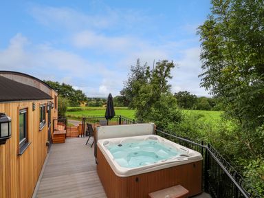 A wooden deck with a hot tub seating and table with umbrella overlooking green fields at The View in Bangor-On-Dee
