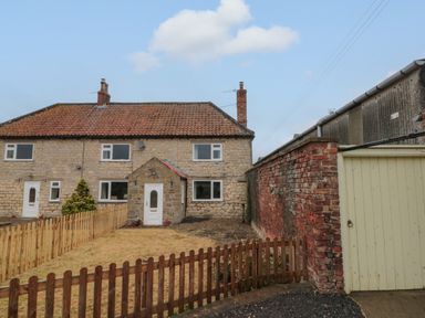 A stone house with a front yard and wooden fences next to a brick wall and gate at Bellmanear Farm Cottage in North Grimston near Malton