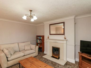 A living room with a beige sofa a wooden bookshelf a fireplace with a mirror above and a TV on a wooden stand at Bellmanear Farm Cottage in North Grimston near Malton