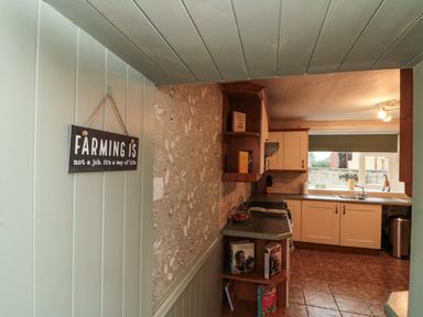 A kitchen with white cabinets, a window above the sink, tiled floor, and a wall sign saying farming is not a job at Bellmanear Farm Cottage in North Grimston near Malton