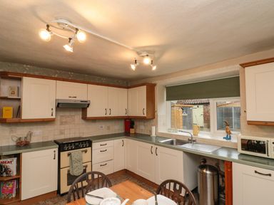 A kitchen with white cabinets a stove a sink and a window with a green blind at Bellmanear Farm Cottage North Grimston near Malton