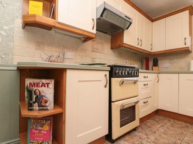 A kitchen corner with cream cabinets beige oven tiled backsplash and cookbooks on shelves at Bellmanear Farm Cottage North Grimston near Malton