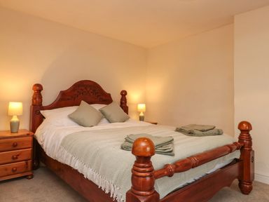 A bedroom with a wooden bed frame two bedside tables with lamps and folded towels on the bed at Bellmanear Farm Cottage in North Grimston near Malton