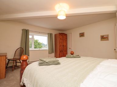 A bedroom with a wooden bed and folded towels on it a wooden chair a wardrobe and a window with green curtains at Bellmanear Farm Cottage North Grimston near Malton