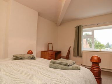 A bedroom with a wooden bed and folded towels on it a wooden desk and chair near a window with green curtains at Bellmanear Farm Cottage North Grimston near Malton