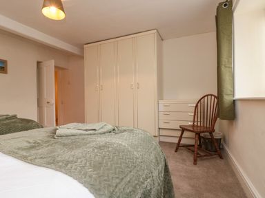 A bedroom with a bed covered by a green blanket towels on the bed a wooden chair next to a window and a wardrobe with drawers at Bellmanear Farm Cottage North Grimston near Malton