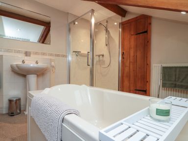 A bathroom with a bathtub holding a candle on a tray a towel on the tub edge a pedestal sink glass shower and a wooden door at Bellmanear Farm Cottage in North Grimston near Malton