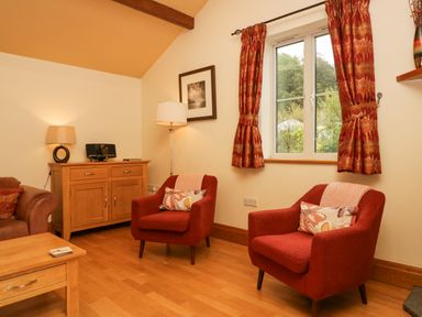 A sitting room with two red armchairs and a window with patterned curtains at Blue Hill House in Ambleside