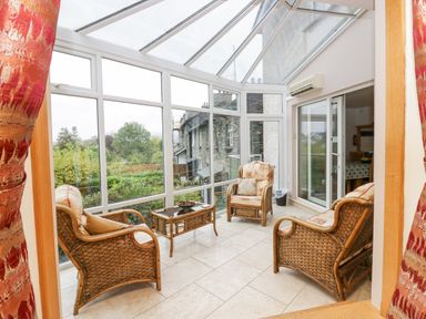 A sunroom with large windows a glass roof wicker chairs and a glass coffee table at Blue Hill House in Ambleside