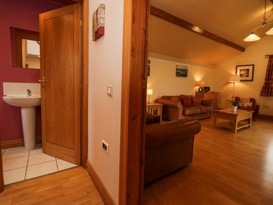 A hallway leading to a bathroom with a sink and a living room with sofas a coffee table and lamps at Blue Hill House in Ambleside