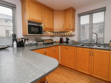 A kitchen with wooden cabinets a microwave kettle sink and windows with blinds at Blue Hill House in Ambleside