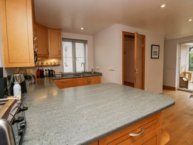 A kitchen with wooden cabinets a gray countertop a sink a window and an open door at Blue Hill House in Ambleside