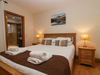 A bedroom with a wooden bed dressed with white and brown linens two bedside tables with lamps and towels on the bed at Blue Hill House in Ambleside